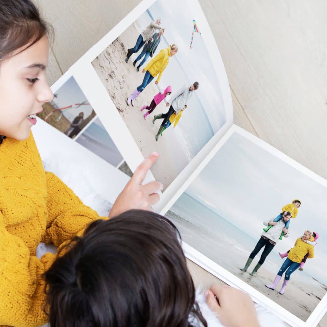 Duas crianças a ver um álbum impresso aberto juntas, uma a apontar para uma fotografia