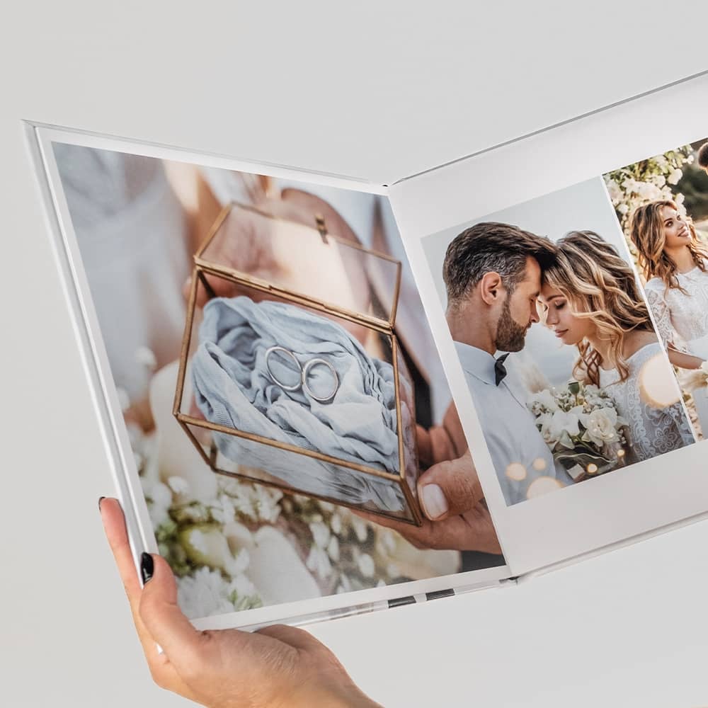 Mão a segurar o álbum impresso aberto numa página dupla com fotografias de casamento