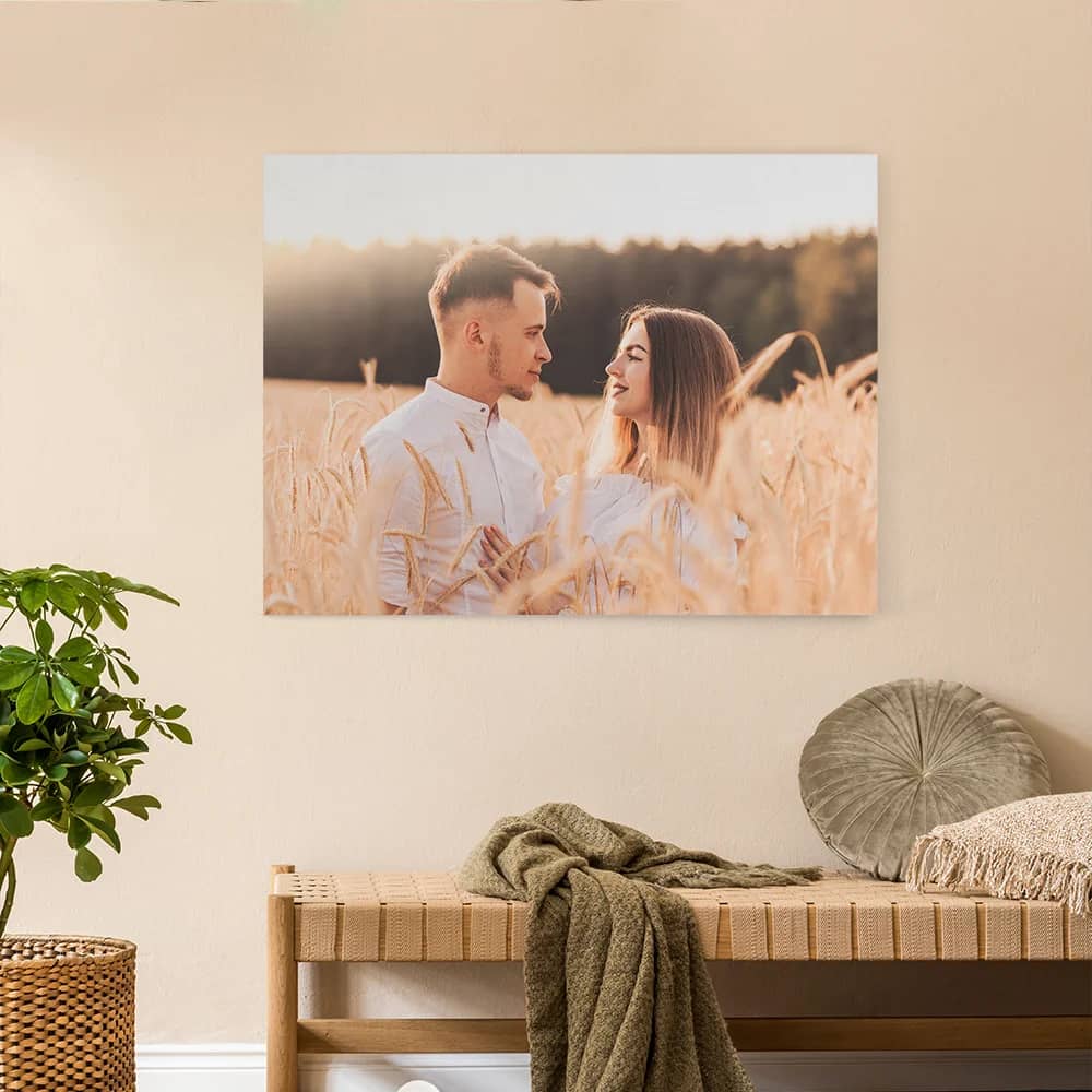 Entrada de uma casa com um banco de madeira, uma manta e um vaso; na parede, uma fotografia grande de um casal num campo dourado