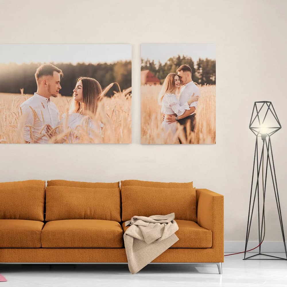 Sala com um sofá cor de mostarda e um candeeiro de pé; na parede, duas fotografias de um casal num campo de trigo
